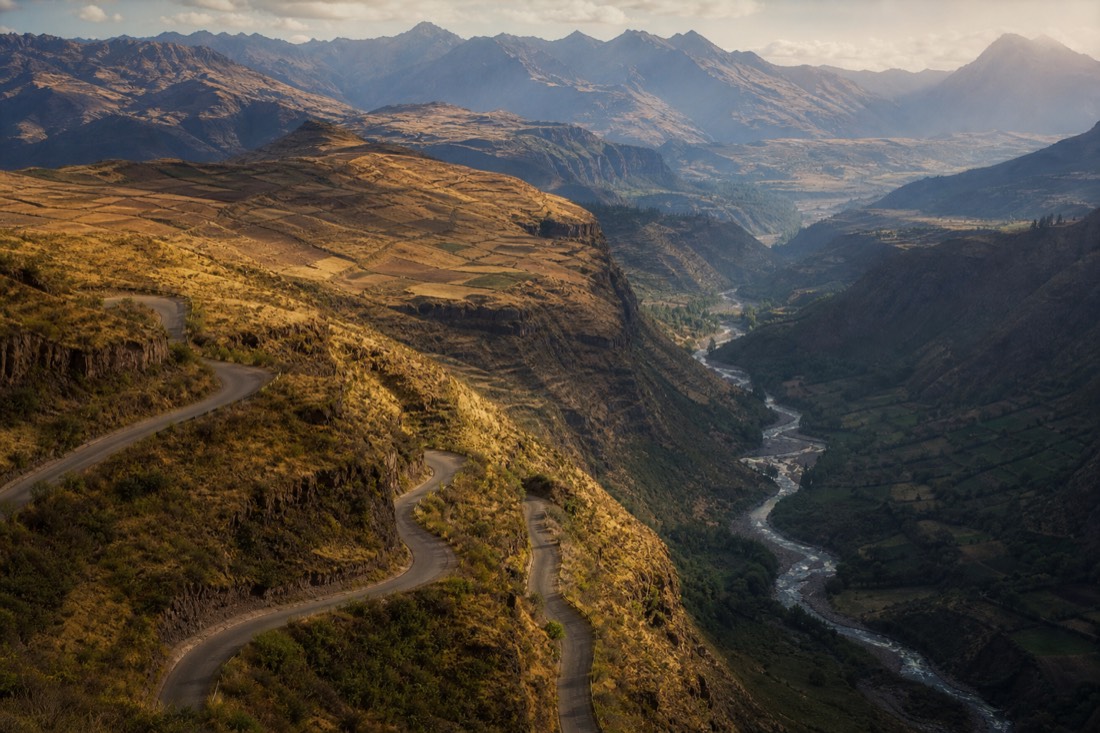 Winding road descending from high Andean plateau into a green river valley