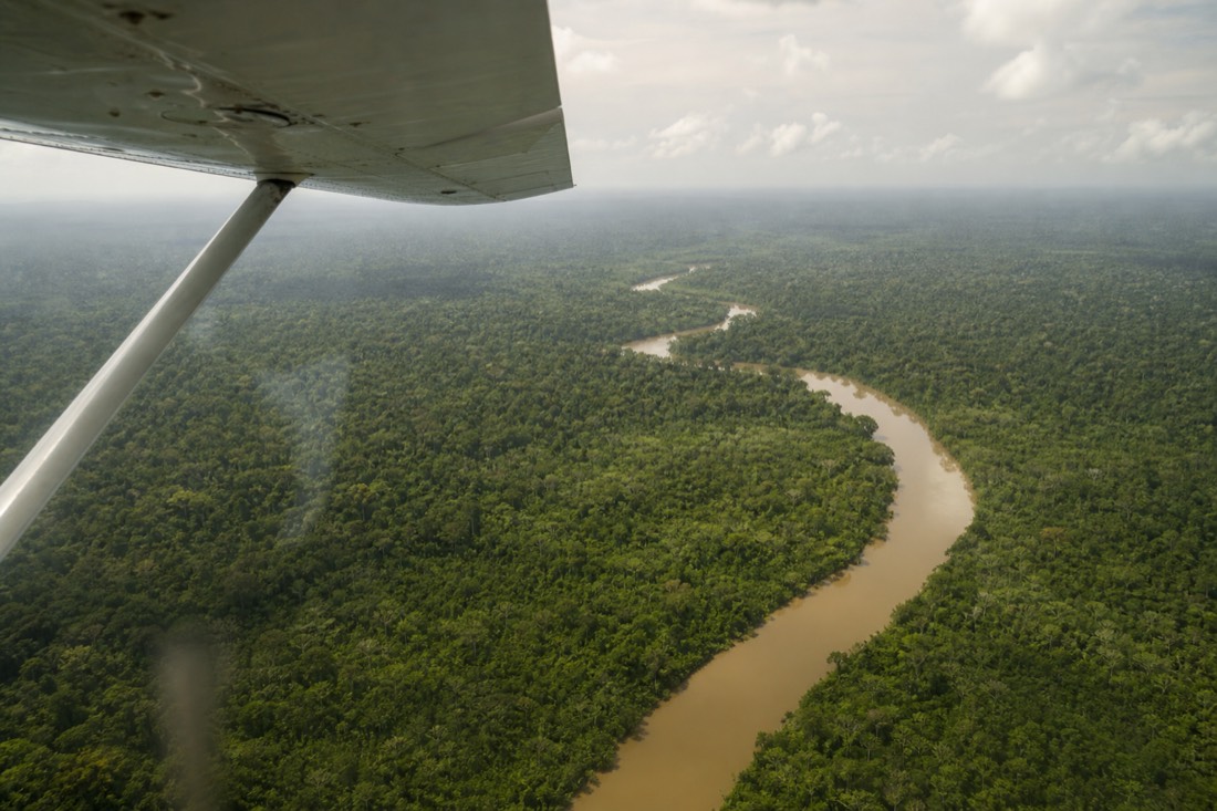 Small propeller plane wing over endless green Amazon rainforest and a winding brown river