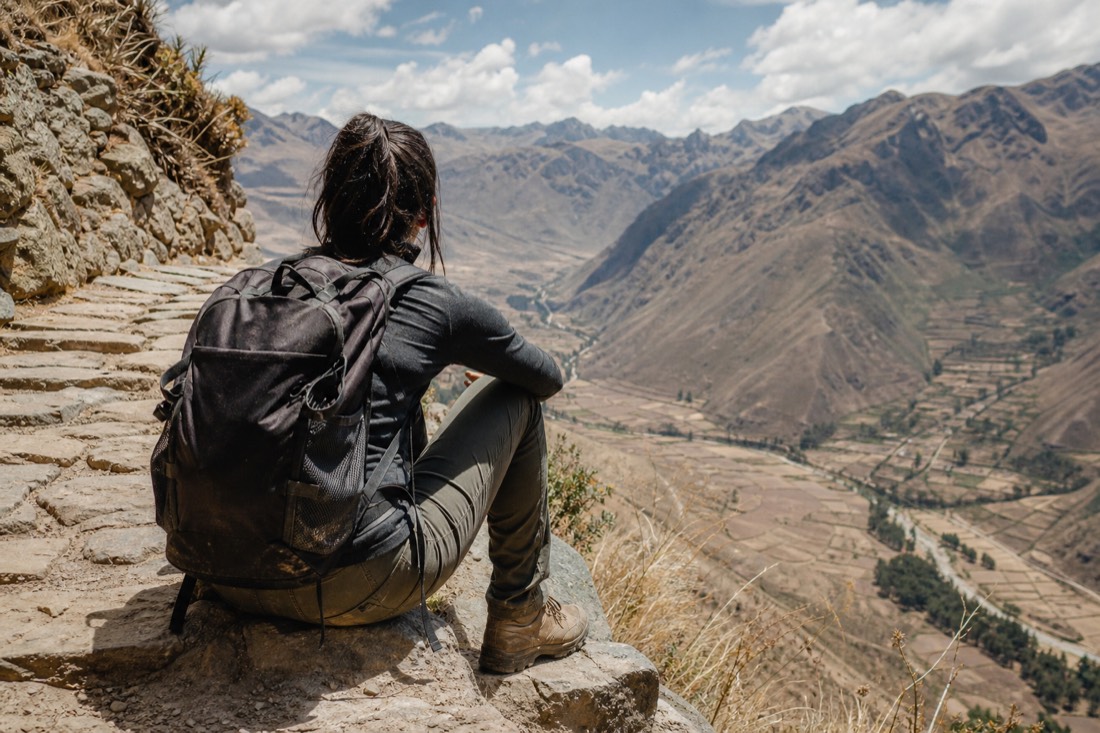 Hiker resting on a stone step of an Inca trail, boots dusty, valley far below