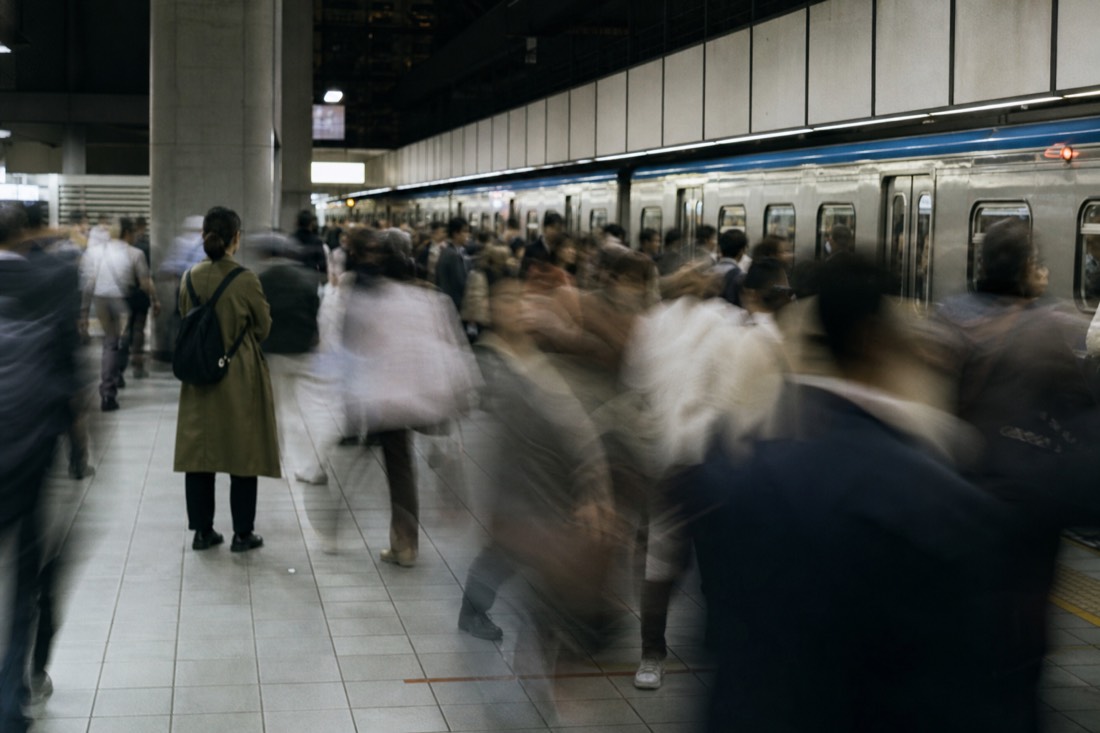 Crowded commuter platform blurred with motion while one figure stands still