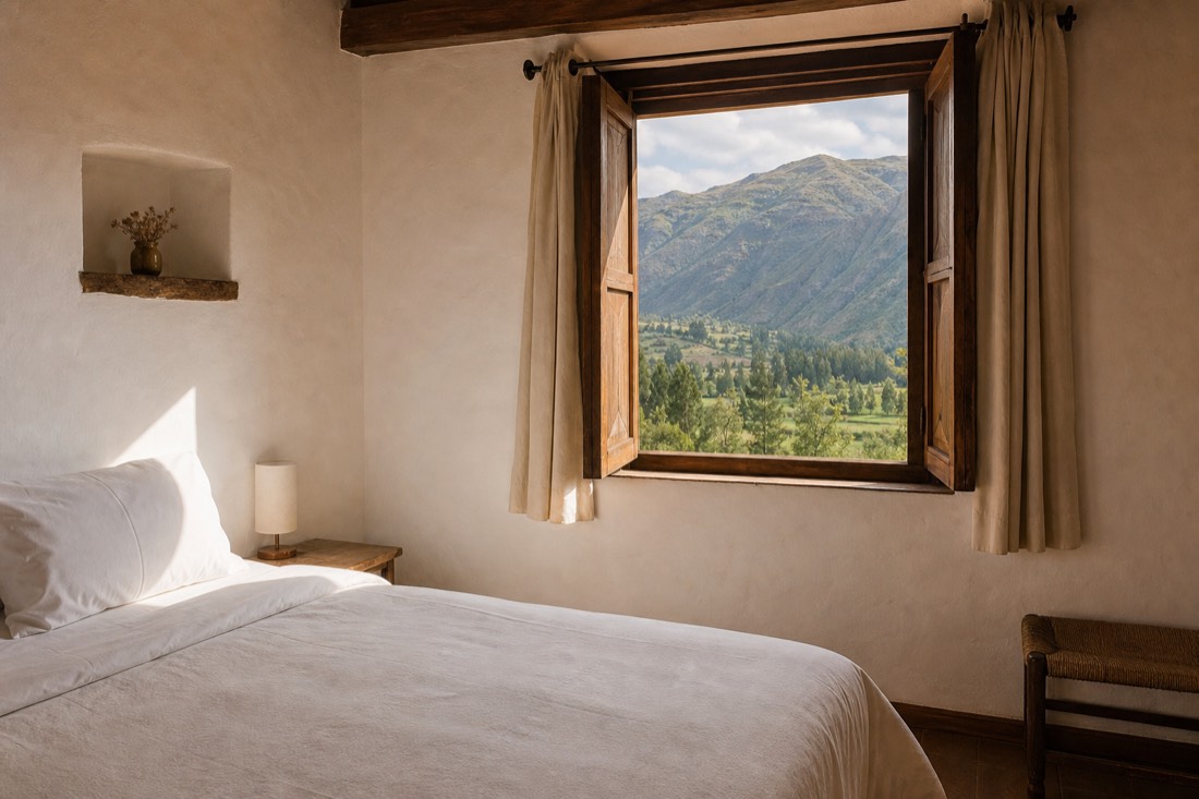 Clean simple retreat room with white bedding and a view of green Andean foothills near Cusco