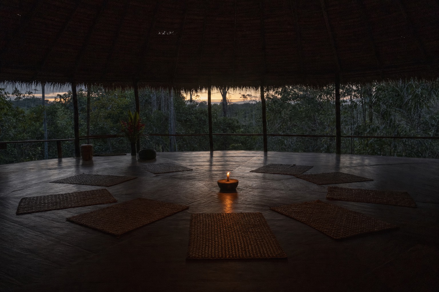 Dim maloca interior at dusk in the Peruvian Amazon with empty ceremony mats and a single candle