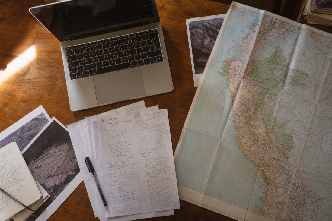 Overhead view of a laptop, printed notes, and a map of Peru spread across a wooden desk