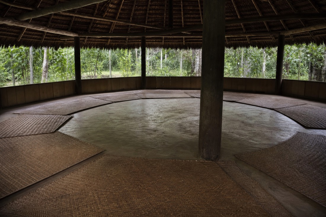 Interior of a round ceremonial maloca with mats arranged in a circle, dim natural light