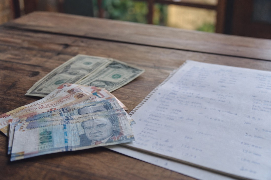 Peruvian soles and US dollar bills beside a handwritten trip budget on a wooden table