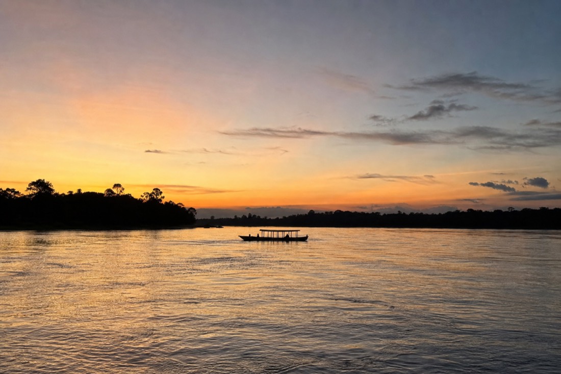 Wide Amazon river with a small wooden boat crossing at dusk near Iquitos