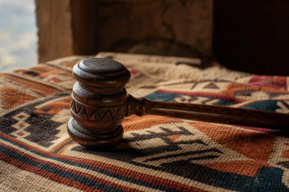 Carved wooden gavel resting on woven Andean textile in warm side light