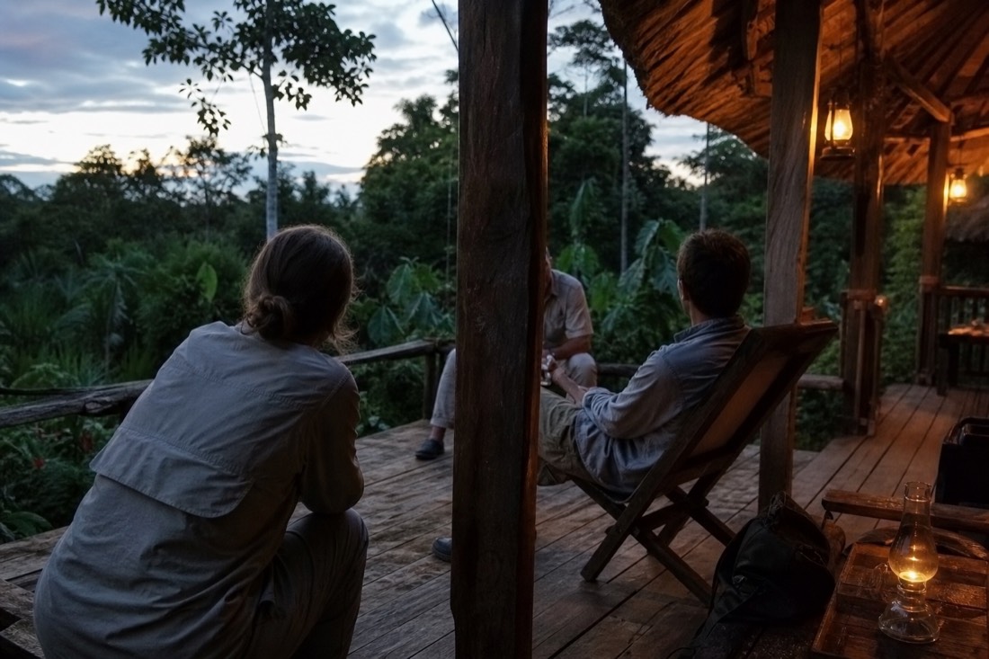 Travelers talking quietly on the wooden deck of a jungle lodge near Iquitos at dusk