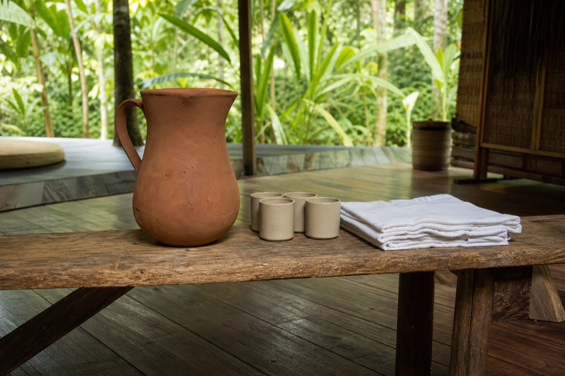 Facilitator's station with water pitcher, cups and folded cloths on a wooden bench inside a jungle retreat space near Tamshiyacu, daytime