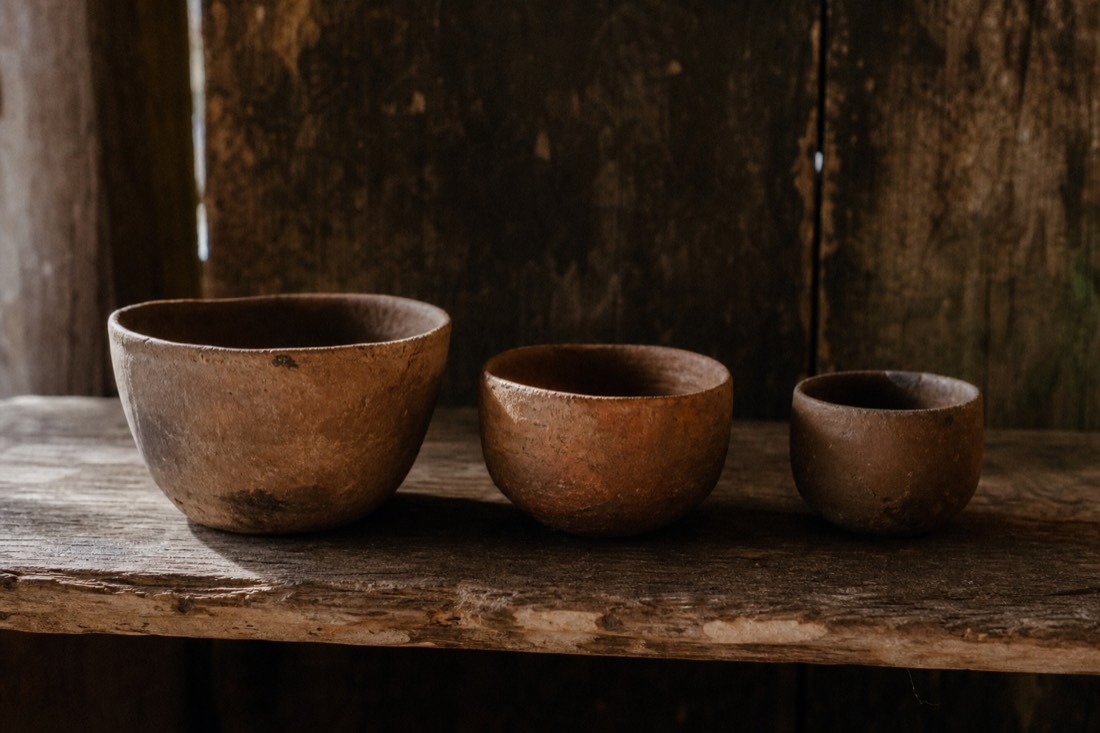 Three small clay cups of different sizes lined up on a rough wooden bench in low light