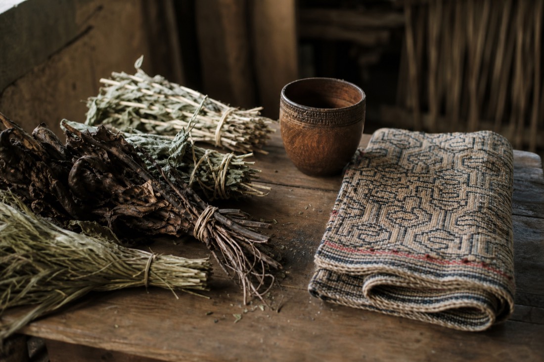 Curandero's table with dried plants, a wooden cup and woven Shipibo-style textile in soft window light, no people visible