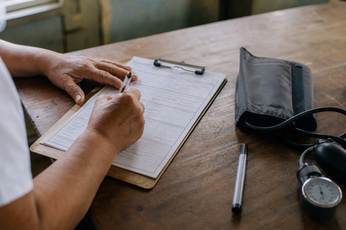Hands completing a paper health questionnaire beside a blood-pressure cuff, the medical screening step before an ayahuasca retreat